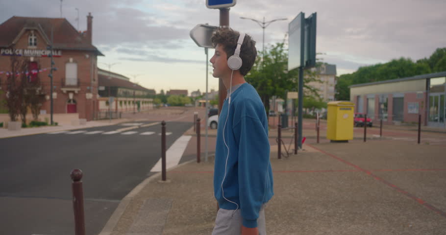 Slow motion footage of young confident teenage boy walking across a zebra crossing while listening to music with headphones at city. Concept pedestrians passing a crosswalk