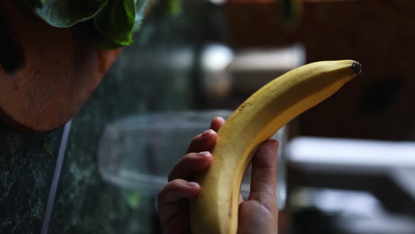Female hands peel off a banana on the background of a blender in the kitchen. vertical video. close-up | Shutterstock HD Video #1108547451
