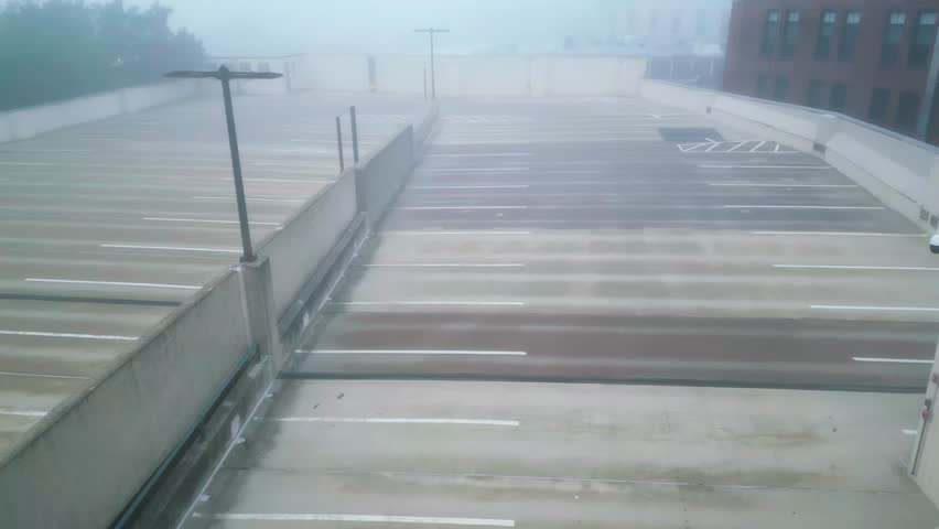 Drone trucking pan across thick foggy upper level of parking garage, white mist