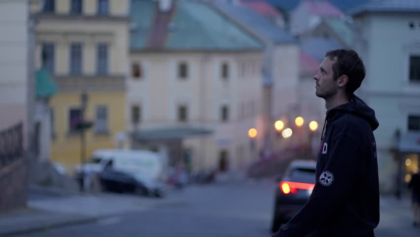 Young man with black Hoodie crossing the street in an old historical town Banska Stiavnica in Slovakia, Europe during a blue hour at dusk, surrounded by historical buildings. 4K, Sony FX3