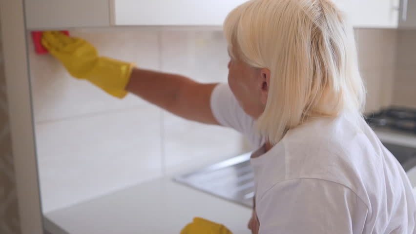 50s senior housewife wearing rubber gloves, involved in wiping kitchen surfaces at home, keeping house neat. Happy professional female cleaning worker mopping dust indoors. High quality FullHD footage Royalty-Free Stock Footage #1108559639