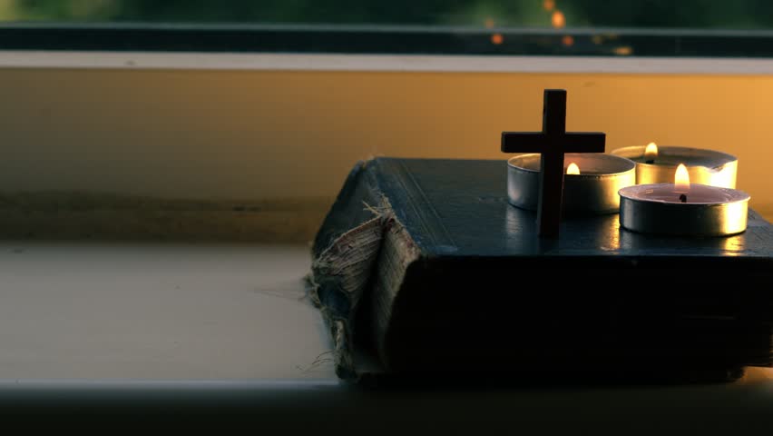 Holy bible with crucifix and tea light candles close up slow motion dolly 4k shot shot selective focus