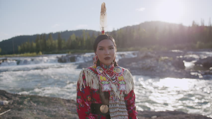 Beautiful Portrait Shot of Young Indigenous Woman wearing traditional North American Native Regalia Tsu'Tina Nation Alberta Canada Down by the river at sunset. Royalty-Free Stock Footage #1108563643