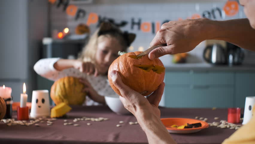 Close-up of father making Jack-o-Lantern while his daughter painting scary face on pumpkin at home, selective focus Royalty-Free Stock Footage #1108564193