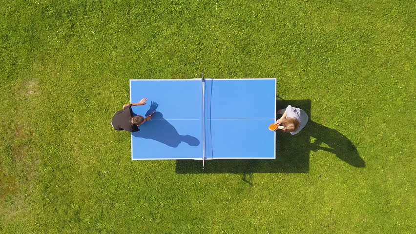 Aerial view people playing ping pong match outdoor. Top view two boys playing table tennis on a green grass lawn. Aerial view outdoor sport
