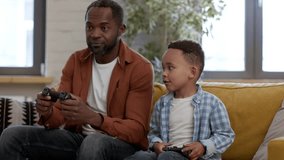 Father and son entertainment. Excited african american dad playing video games with his little kid on gamepad using joysticks, babysitting at home, tracking shot, slow motion, free space - Powered by Shutterstock - Get 15% off with code: PIKWIZARD15