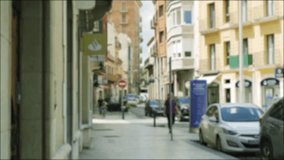 Pedestrians with children walk along the street of the Spanish city, cars drive, cars are parked nearby. Blurred background video.