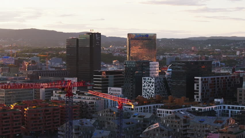 Group of modern high rise buildings in urban neighbourhood at sunset. Tower cranes on construction site. Metropolis at golden hour. Oslo, Norway