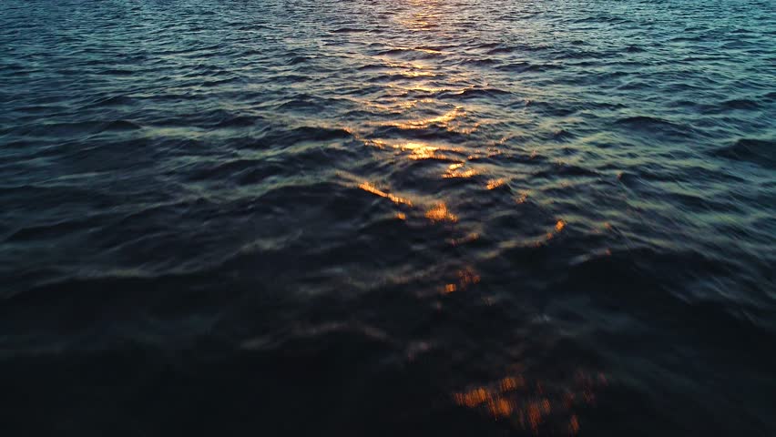 Aerial dolly push in tilt up to setting sun over ocean ripple texture 