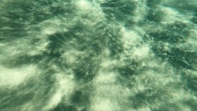 Underwater and then surface slow motion underwater video of sunlight waves playing on the white sandy bottom at the turquoise shallow water of Elafonissi Beach. Crete. Greece