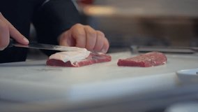 Professional chef slices fat on meat with his sharp knife in slow motion.
