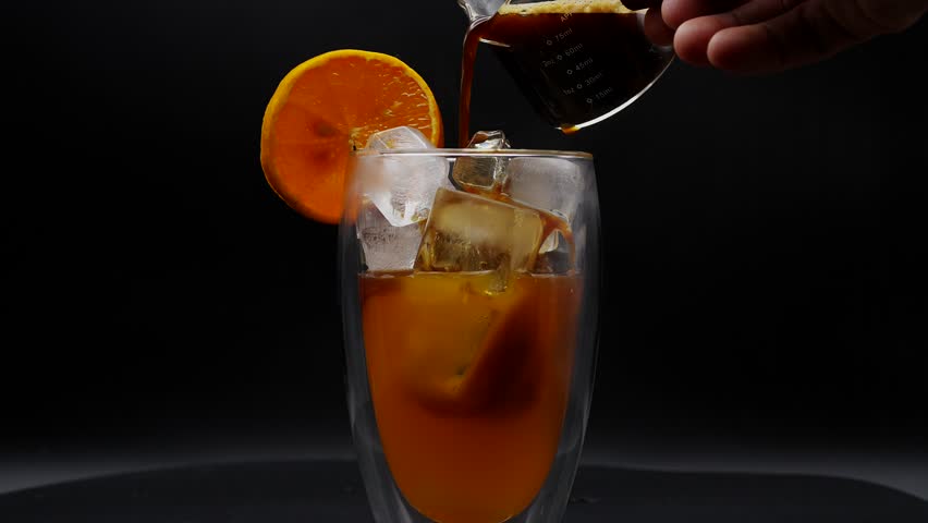 Coffee pouring into orange juice iced glass rotating. Royalty-Free Stock Footage #1108579329