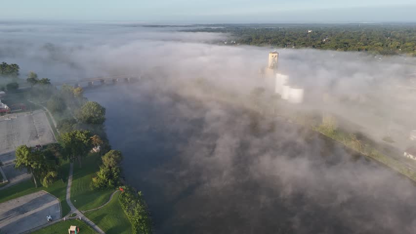 A foggy aerial view of the Saginaw River with silos peeking above the fog in the distance.  	