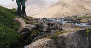 Mountain stream, stream crossing, feet in sneakers, slow motion. Arashan. Legs of man in sneakers, crossing stream over stones. Cinematic. Cinematic ecological amazing nature. Concept of peaceful life