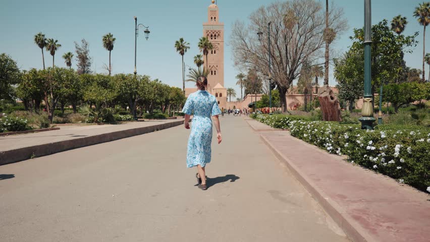 Young caucasian woman in a dress walking towards Koutoubia Mosque, Marrakech, Morocco.