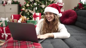 Young beautiful hispanic woman having video call sitting on floor by christmas tree at home