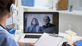 online consultation, young female doctor with a headset advises an elderly man and woman via video link on a laptop in a medical office