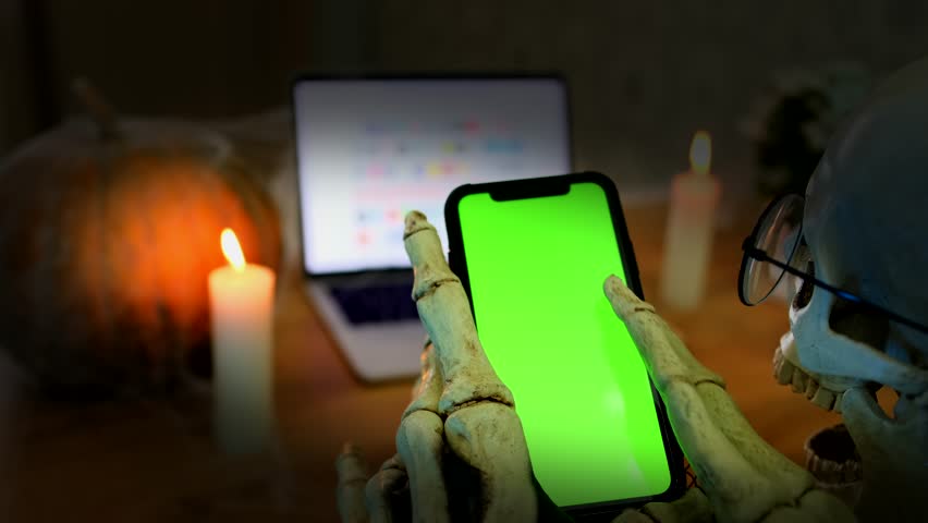 Close up, hands in skeleton costume holding for smartphone with chromakey watching video online platform, networks. Dark vignette. Halloween party, social media.