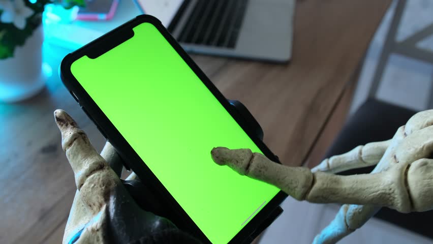 Scary skeletal hand with bony fingers touches the screen with a smartphone stroking the screen with chromakey. Man in skeleton costume becomes obsessed with messaging strangers online