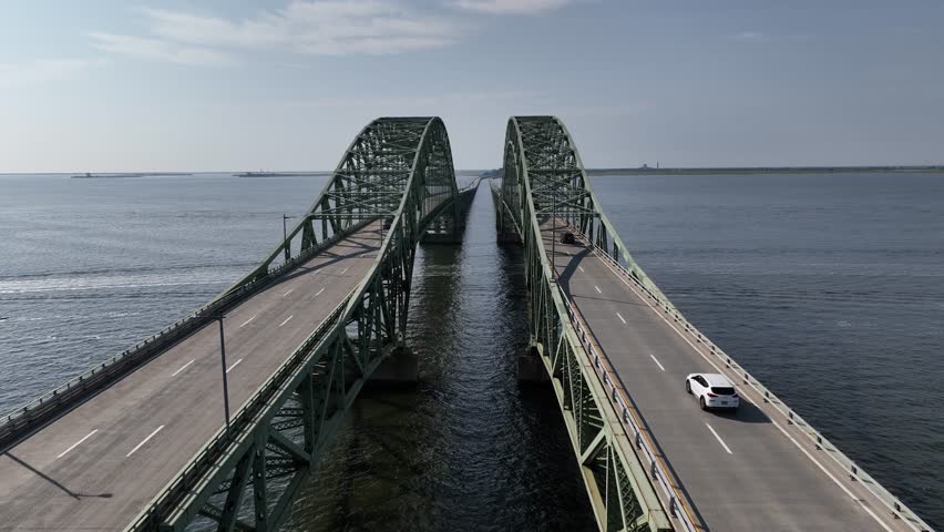 An aerial view of the Great South Bay Bridge and the Robert Moses Causeway on a beautiful day. The camera dolly in between the roads and the double arches as cars drive by. Royalty-Free Stock Footage #1108594969