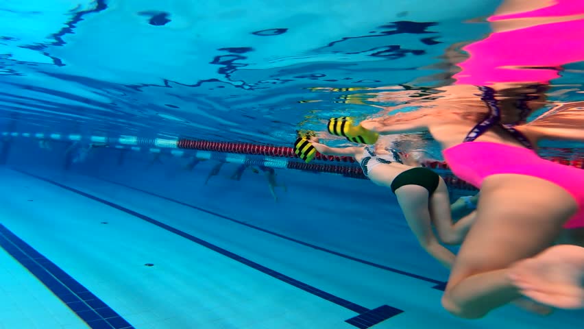 Two young girls are training  in a pool with the freestyle legs kicking. Underwater rear view.