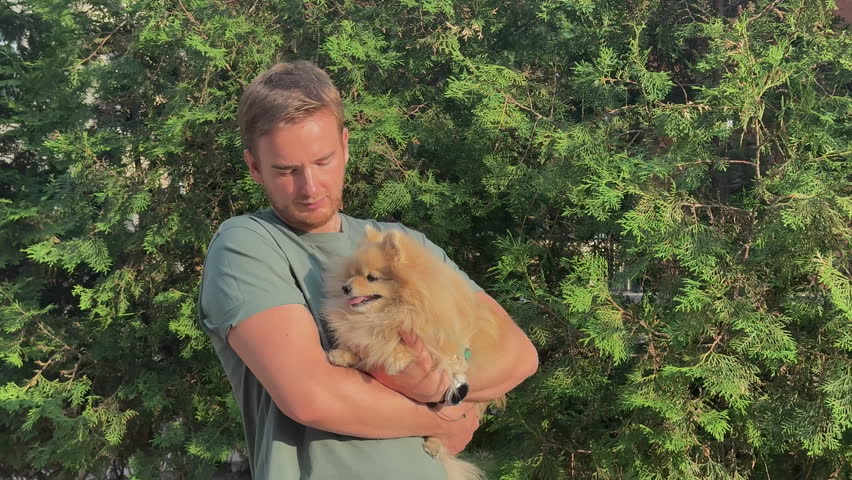 portrait of young man with a dog, pomeranian spitz in her arms in the park
