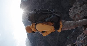Man climbing mountain with trekking poles. Male hiker standing on top of mountain, admiring beautiful landscapes, travelling on autumn vacation. Hiking, sport concept. Vertical video cinematic