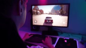 Closeup view from shoulder of unrecognizable male gamer driving race video game on pc computer in dark room. Close-up of young man playing car racing simulator at home. Shooting in slow motion.