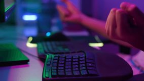 Close-up hands of unrecognizable gamer gesturing win with hands after winning game, pushing keyboard buttons playing online video game on dark room with neon led lights. Shooting in slow motion.