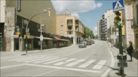 Cars are driving at a green traffic light down the street of a Spanish city, a pedestrian is waiting at a traffic light, people are walking along the sidewalk. Blurred background video.