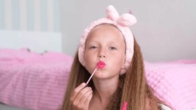 A girl sits near the bed and paints her lips. The child looks at the camera and applies lip balm. - Powered by Shutterstock - Get 15% off with code: PIKWIZARD15