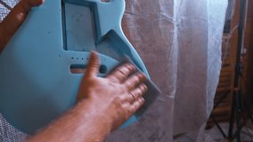 Man sanding blue body of electric guitar after painting. 4k video footage UHD 3840x2160