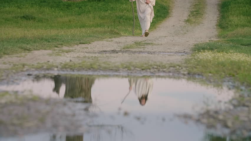 Jesus as a Pilgrim walking slowly on a muddy road. Front view Royalty-Free Stock Footage #1108612771