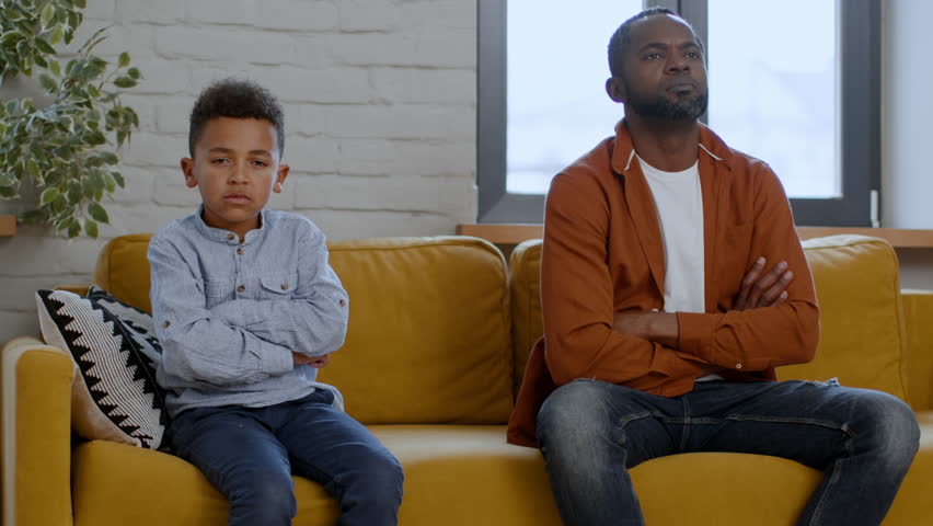 Kids and parents gap. Upset offended african american father and his preteen son sitting apart on sofa, looking at each other and turning backs after quarrel, free space Royalty-Free Stock Footage #1108615389