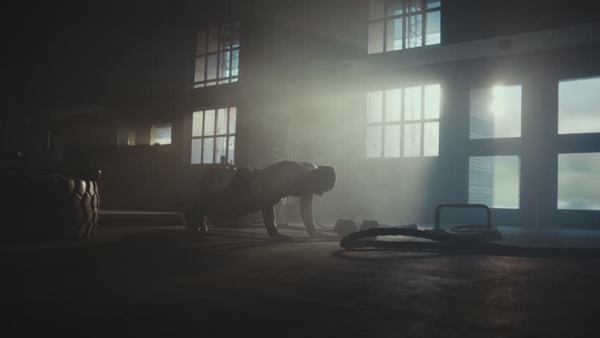 Slow-motion shot of a handsome young man in gym doing push-ups on the floor. Tyres and dumbbels are kept aside Royalty-Free Stock Footage #1108632011