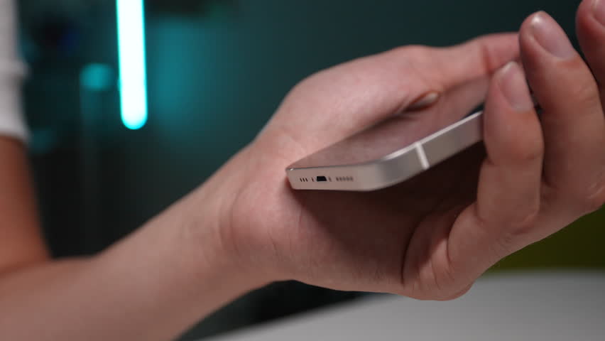 Detail cropped shot of unrecognizable man plugging and unplugging lightning cable into smartphone connector to charge sitting at home table. Closeup male hands connecting cable for transfer data.