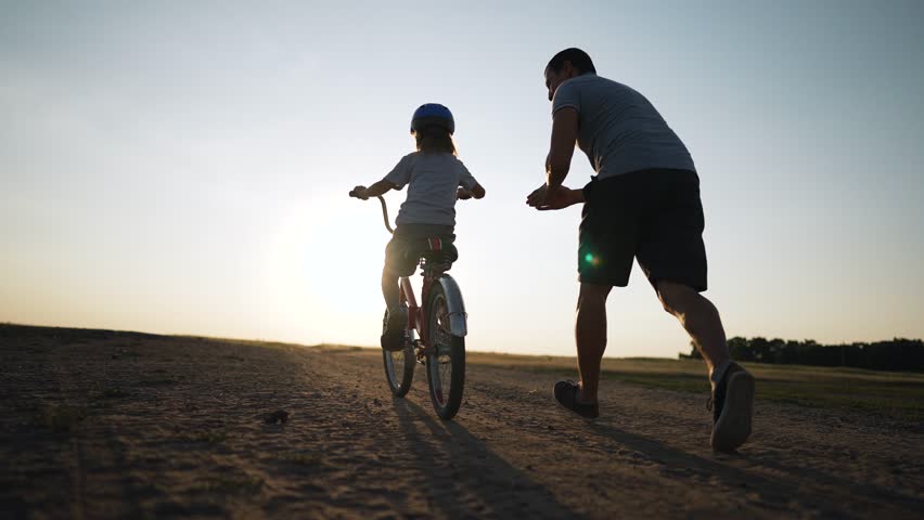 Father's Day.Father teaches daughter to ride bicycle wearing safety helmet.child learn to ride bicycle in park at sunset.Happy family concept and dream.Active father teaches child to ride bike in park Royalty-Free Stock Footage #1108639337