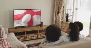 Biracial family watching tv with rugby ball on flag of england on screen. Communication technology, flags and sports, digital composite video.