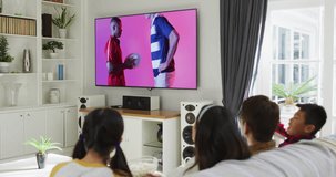 Asian family watching tv with diverse male rugby players with ball on screen. Communication technology and sports, digital composite video.