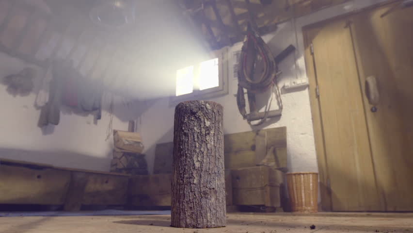Man walks trough the door and hammers down the axe in to the small log in the middle of a cabin, footage in slow motion.