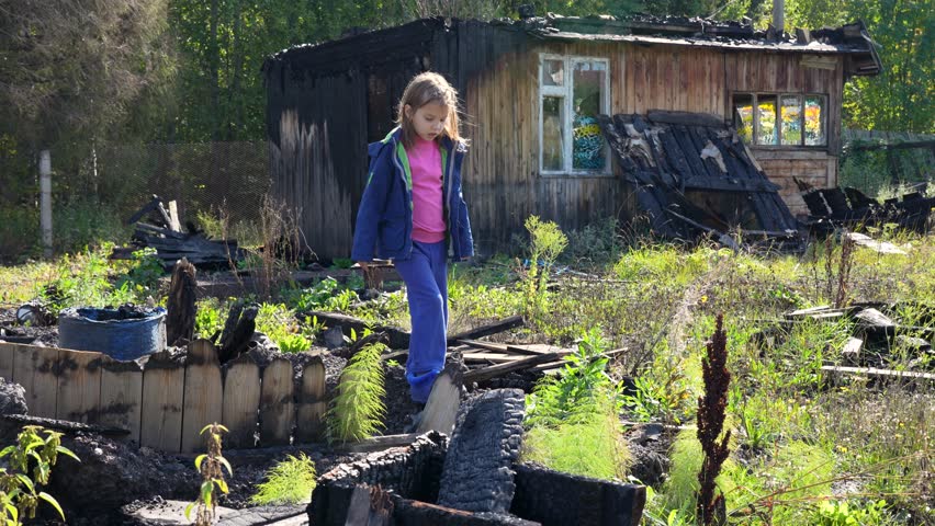 A child and destroyed house. Little girl near the burnt home after bomb attack. A child in a war-torn house. Consequences of the war