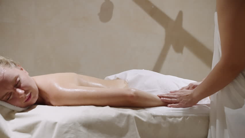 Masseuse massages female arms in spa hammam. Anti aging and anti cellulite therapy by scrubbing, peeling in sauna. Woman lies relaxing on table, gets full body skin treatment. Royalty-Free Stock Footage #1108646391