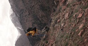 Adventurous male wears yellow jacket and black backpack. Journey towards remote top of the mountain, concept hiking and exploration. Vertical video cinematic. Genuine outdoor lifestyle autumn vacation