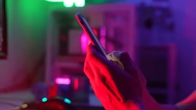 Close-up cropped shot of unrecognizable young man using typing smartphone on dark room with neon bokeh lights. Closeup male hands typing text or shopping online, reading social media or internet. - Powered by Shutterstock - Get 15% off with code: PIKWIZARD15