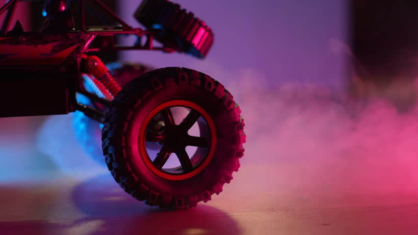 Closeup of radio-controlled toy car driving, tugging, spinning wheels on floor in dark living room on background of smoke and neon lights. Concept of children toys. Shooting in slow motion.