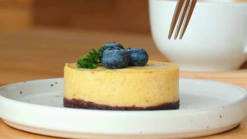 Man Hand Takes Fresh Lemon Cheesecake Slice. Closeup of delicious lemon cheesecake slice being lifted by hand. Gourmet dessert on plate, with creamy cheese, blueberry, and fork.