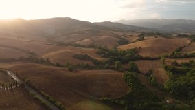 Drone footage slowly flies over an empty field in Tuscany, revealing the beautiful rural landscapes of Italy in the summer with the stunning sunlight. The background features more hills and mountains.
