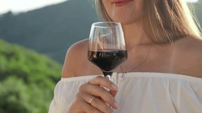 Closeup video clip, showcasing an elegant lady sipping red wine from a glass on a charming villa terrace, set against the stunning backdrop of mountainous landscapes.