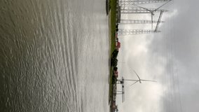 River cruising through South Holland in the Netherlands. Views of the Dutch landscape moving past an industrial area with wind turbines. Located in Nijmegen, Netherlands on the Waal River.