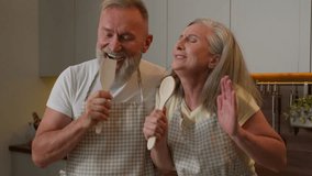 Retired middle aged Caucasian family old couple sing domestic karaoke at home kitchen happy funny spouses gray haired man husband and wife woman singing song at kitchenware spoons dancing fun cooking - Powered by Shutterstock - Get 15% off with code: PIKWIZARD15